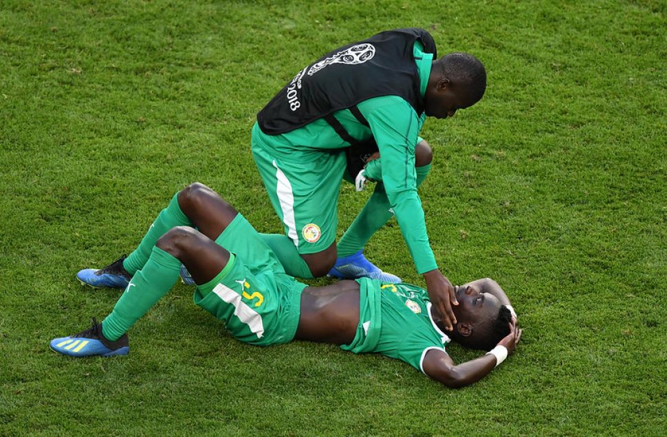 塞內加爾中場Idrissa Gana Gueye賽後躺在場上，隊友前來安慰。（AFP授權）